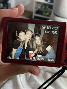 a person holding up a small camera with two girls on it's screen in front of a bed