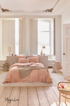 a bedroom with white walls and wooden flooring has a pink comforter on the bed