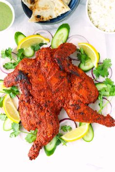 whole roasted tandoori chicken on a plate with cucumbers and lemon wedges