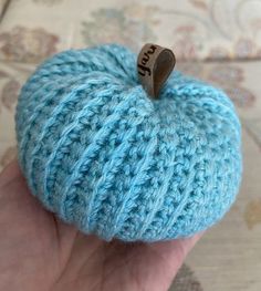 a small blue crocheted apple sitting on top of a table next to a person's hand