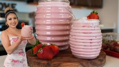 a woman in a dress is holding a drink and strawberries on the table next to two large pink vases