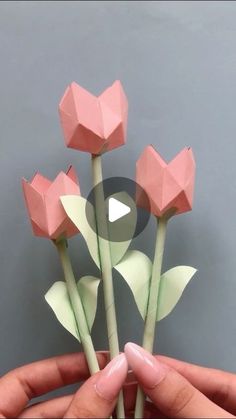 someone is holding three paper flowers in their hands, one pink and the other green