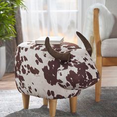 a cow footstool sitting on top of a rug next to a chair and potted plant