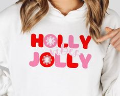 a woman wearing a white sweatshirt that says holly jolly