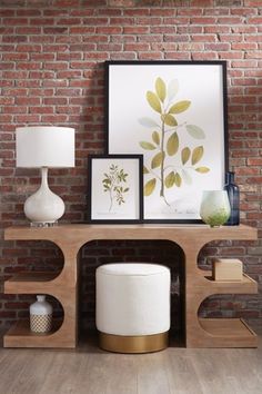 a wooden shelf with two lamps and pictures on it next to a brick wall in a living room