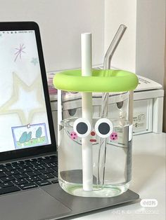 a laptop computer sitting on top of a desk next to a glass cup with two straws in it