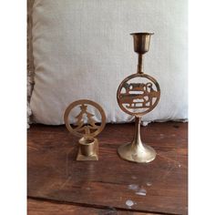 two brass candlesticks sitting next to each other on a wooden table with a pillow in the background