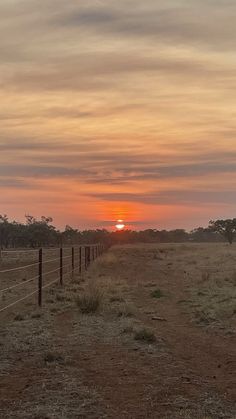 the sun is setting behind a fence in an open field with grass and trees on either side