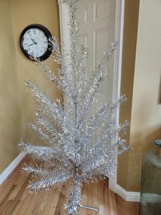 a silver christmas tree sitting on top of a hard wood floor next to a clock