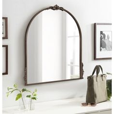 a mirror sitting on top of a white counter next to a vase and plant in front of it