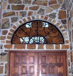 two wooden doors with wrought iron designs on the side of a stone wall and above them is an arched window