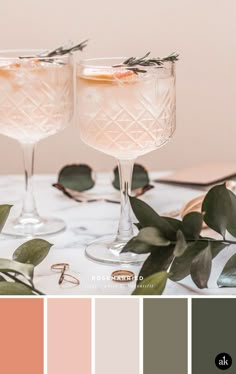 two glasses filled with drinks sitting on top of a table next to leaves and greenery