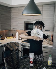 a man with dreadlocks is holding a paper fan in his hand while standing at the kitchen counter