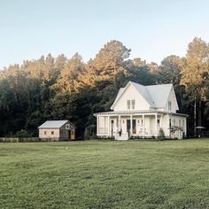 a large white house sitting in the middle of a lush green field next to trees