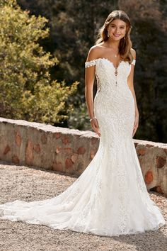 a woman in a white wedding dress standing on a stone wall with trees in the background