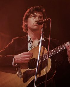 a man holding a guitar while standing in front of a microphone