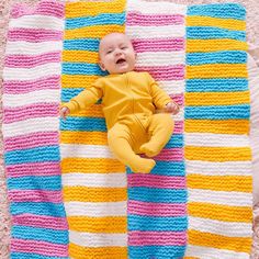 a baby laying on top of a multicolored crocheted blanket in the shape of a rectangle