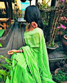 a woman in a green sari sitting on a wooden deck next to potted plants