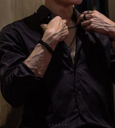 a man adjusting his tie while standing in front of a mirror and wearing a black shirt