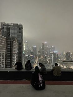 three people sitting on a ledge looking out at the cityscape and skyscrapers