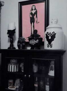 a black and white shelf with a painting on it next to candles, jars and other items