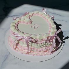 a heart shaped cake with pink and white icing on a marble tableclothed surface