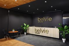 an office with black walls and wooden flooring, plants on the desk in front of the reception counter