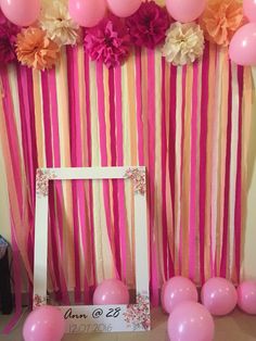 pink and yellow balloons are hanging from the wall near a photo frame with flowers on it