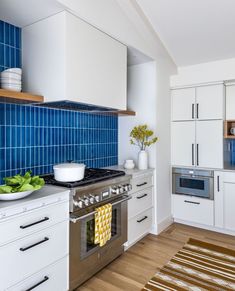 a kitchen with white cabinets and blue tile backsplash, stainless steel stove top oven and dishwasher