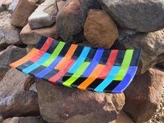 a multicolored striped glass plate sitting on top of a pile of rocks next to a rock wall