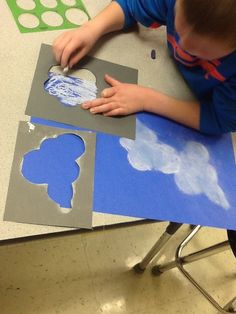 a young boy is working on some paper cut outs with blue and white clouds in the background