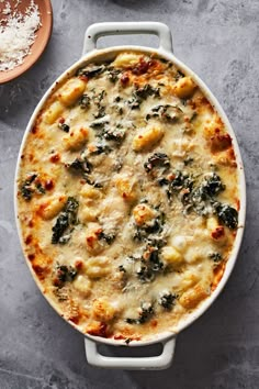 a casserole dish with cheese, spinach and other toppings on a table