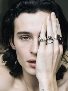 a shirtless man holding his hands to his face with two rings on each hand