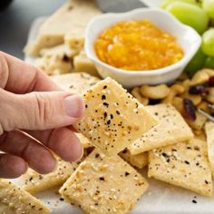 someone is picking up crackers from a platter with fruit and nuts on it