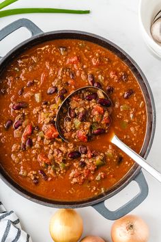 a pot filled with chili and beans on top of a white table next to onions