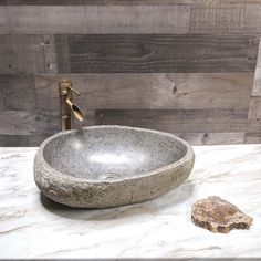 a stone bowl sink sitting on top of a marble counter next to a wooden wall