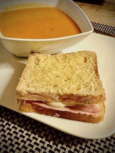 a white plate topped with a sandwich next to a bowl of soup