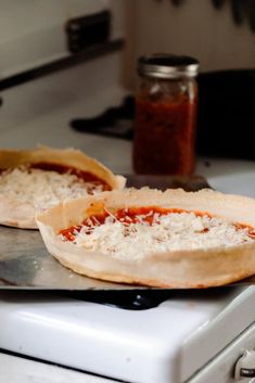 two uncooked pizzas sitting on top of a stove next to each other