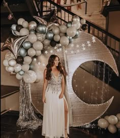 a woman in a white dress standing next to some balloons and silver stars on the wall