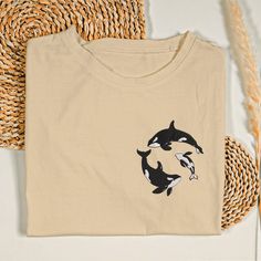 two orca whales on a tan t - shirt sitting next to some straws