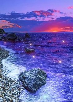 the beach is covered in rocks and pebbles as the sun sets over the ocean behind it