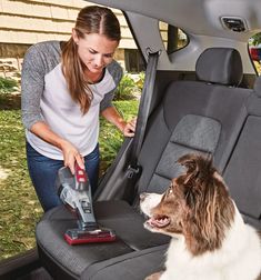 a woman vacuuming the back seat of a car with a dog sitting next to her