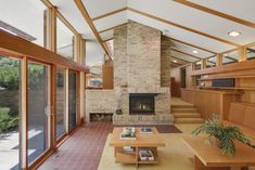 a large living room with brick fireplace and wooden furniture in the center, surrounded by glass doors