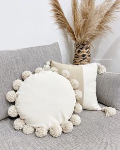 a white pillow sitting on top of a couch next to a vase filled with dry grass