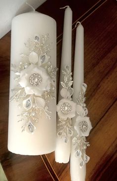 two white candles decorated with flowers and pearls on top of a wooden table next to each other