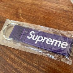 a purple supreme keychain sitting on top of a wooden table next to a plastic bag