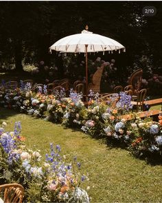 an umbrella in the middle of a flower garden with chairs and tables set up around it