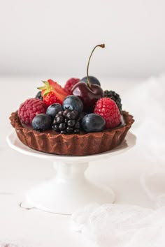 a chocolate tart topped with berries and blackberries on a white cake platter