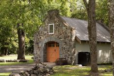 a small stone building with a red door in the middle of some trees and grass