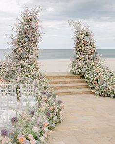 an outdoor ceremony set up on the beach with white chairs and flowers in the foreground